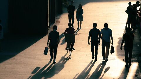 Personen Menschen im Gegenlicht gehen über einen Platz.
