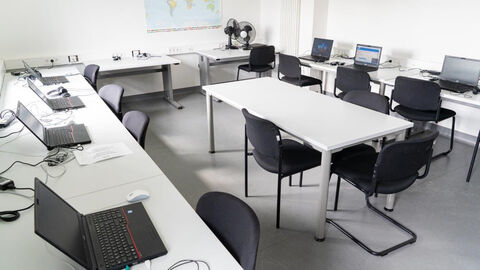 ELIS Raum In einem Seminarraum befinden sich Tische mit Notebooks, Stühle und eine Tafel.